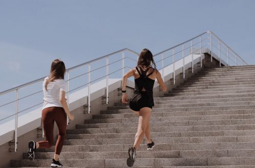 Two women running up stairs outdoors, embodying fitness and wellness.